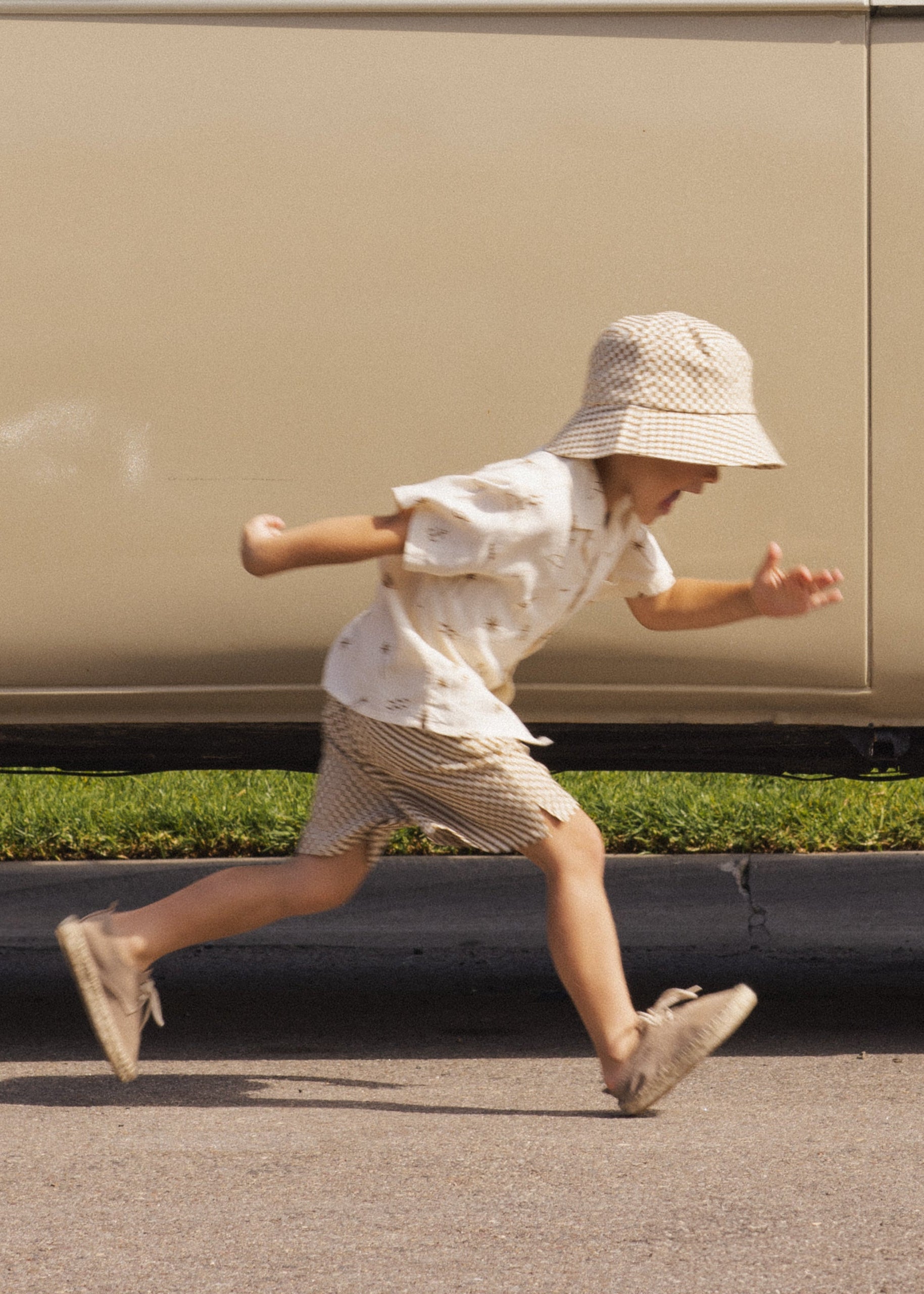 Child running on a road wearing a white shirt, striped skirt, and sun hat.