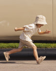 Child running on a road wearing a white shirt, striped skirt, and sun hat.
