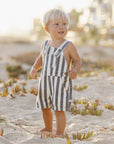 Child in a striped romper standing on a sandy beach with blurred background