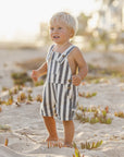 Child in a striped romper standing on a sandy beach with blurred background