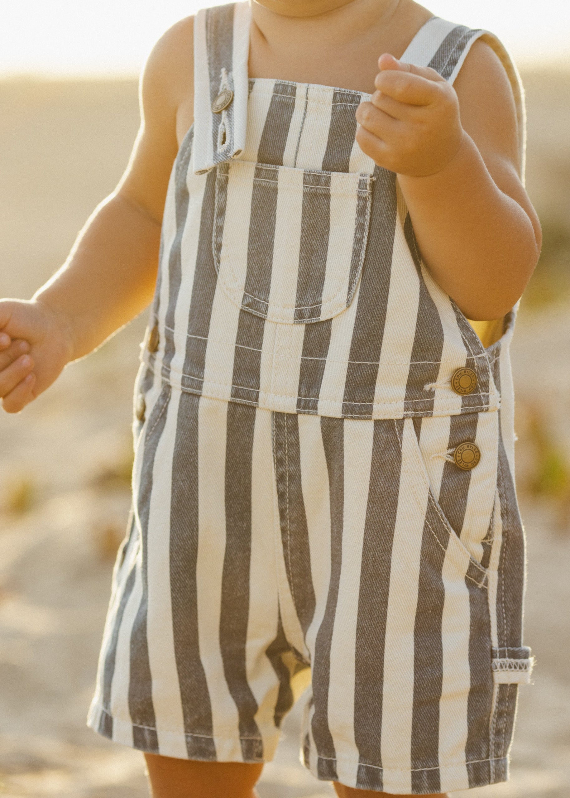 Child wearing striped overalls on a beach