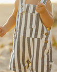 Child wearing striped overalls on a beach