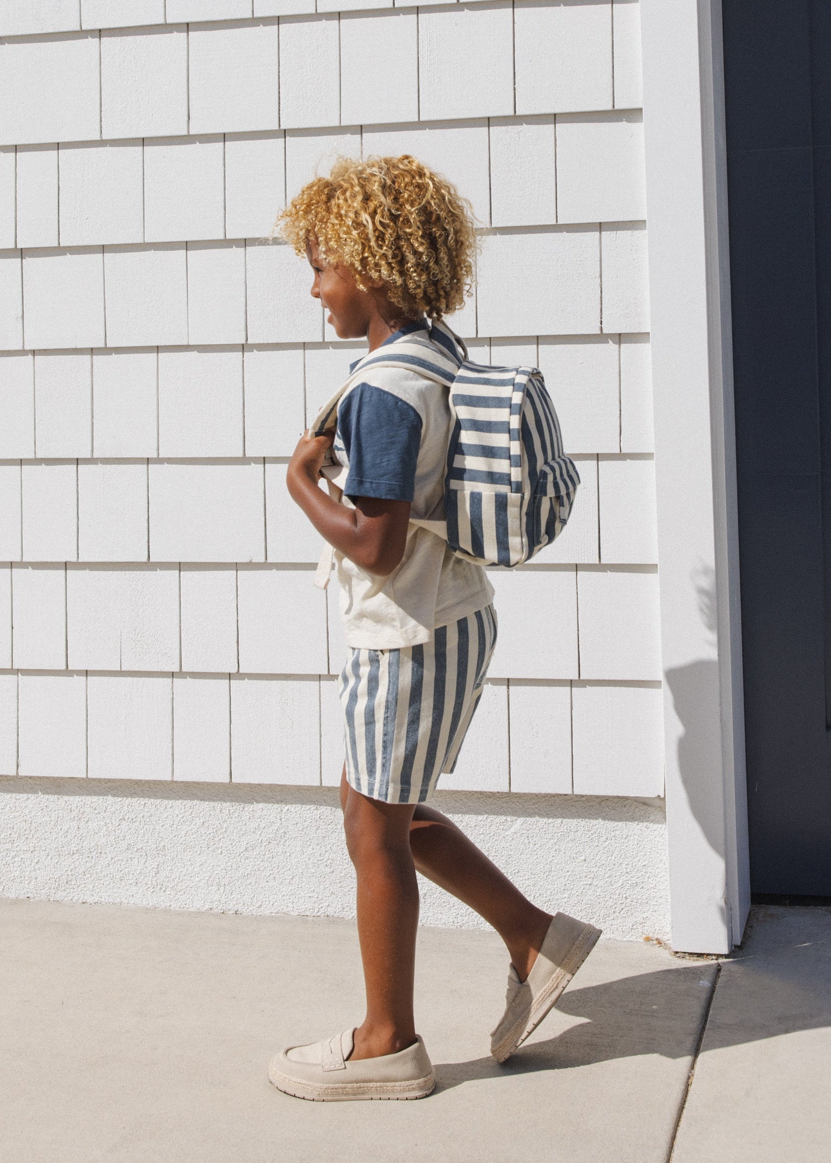 Person wearing a striped outfit with a backpack walking against a tiled wall.