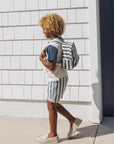 Person wearing a striped outfit with a backpack walking against a tiled wall.