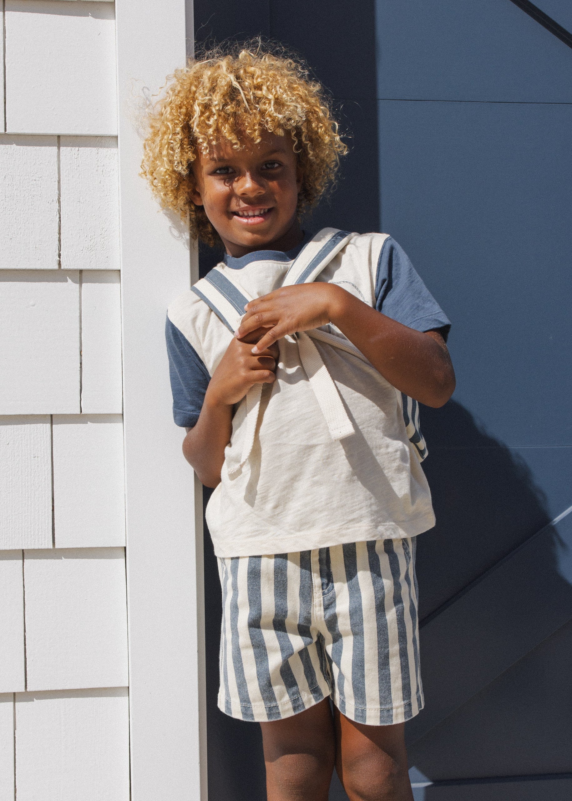 Child wearing a striped outfit standing against a white and blue wall.