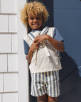 Child wearing a striped outfit standing against a white and blue wall.