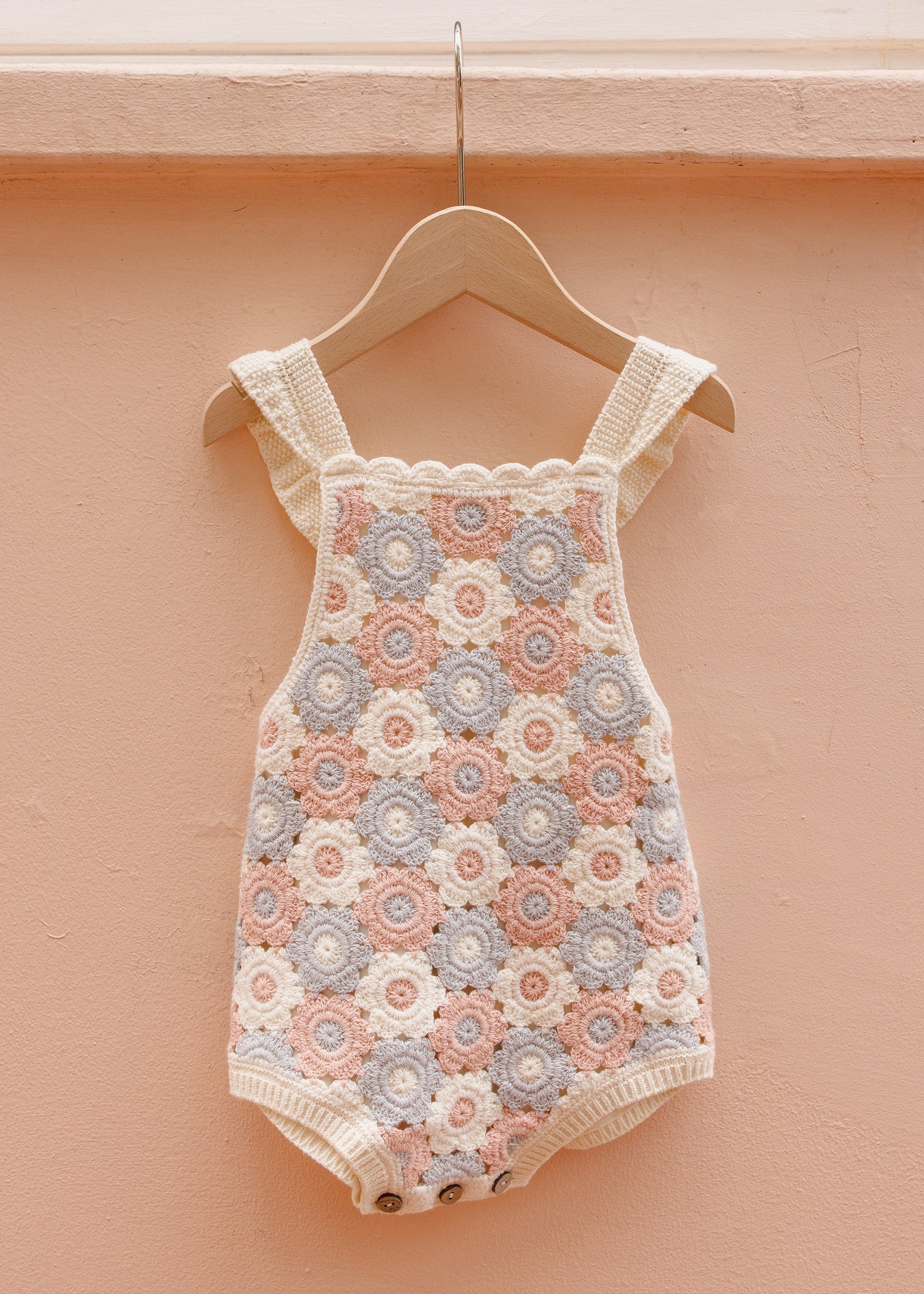 Baby romper with floral pattern on a hanger against a peach-colored wall