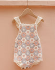 Baby romper with floral pattern on a hanger against a peach-colored wall