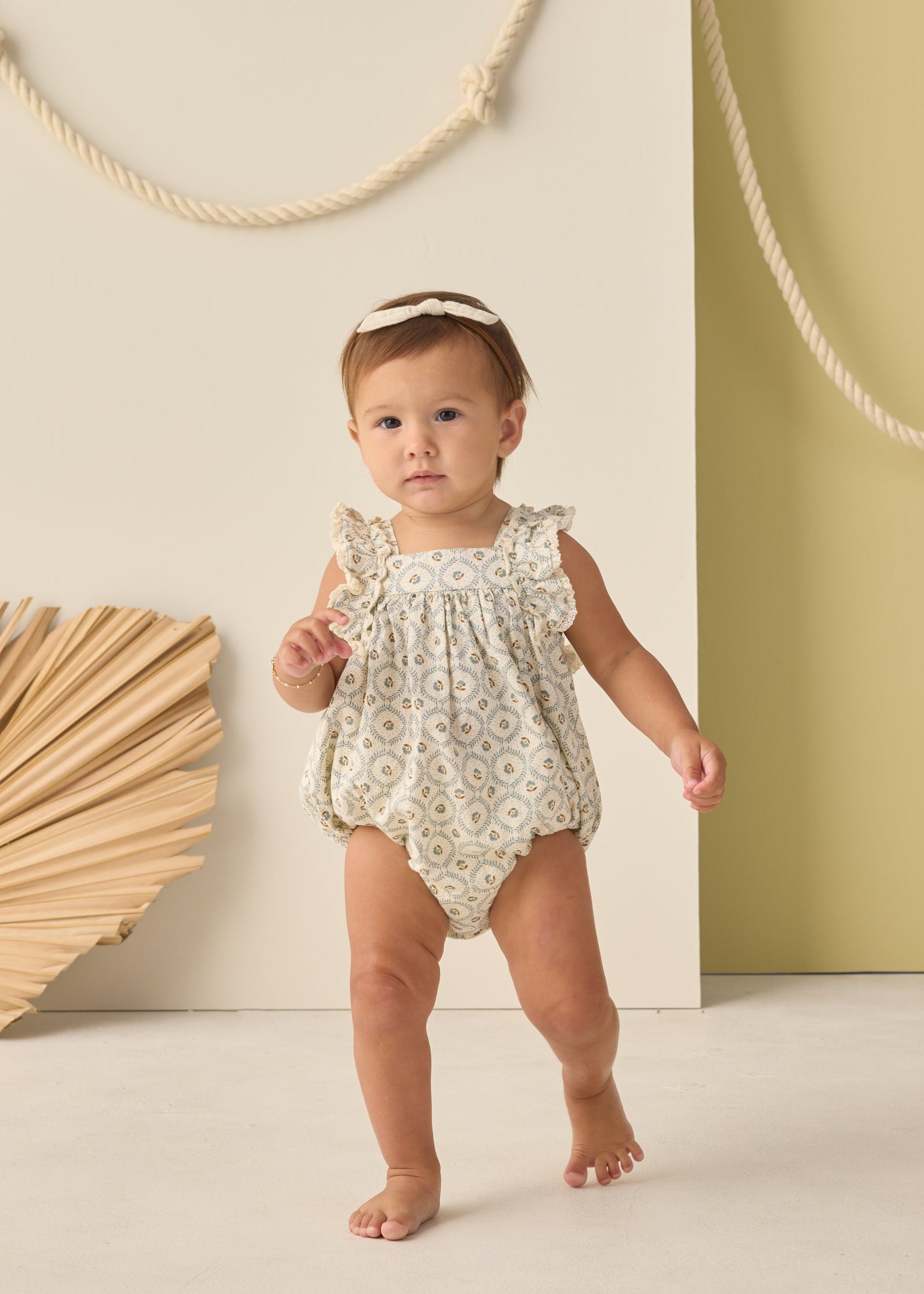 Baby in a floral romper standing against a neutral background