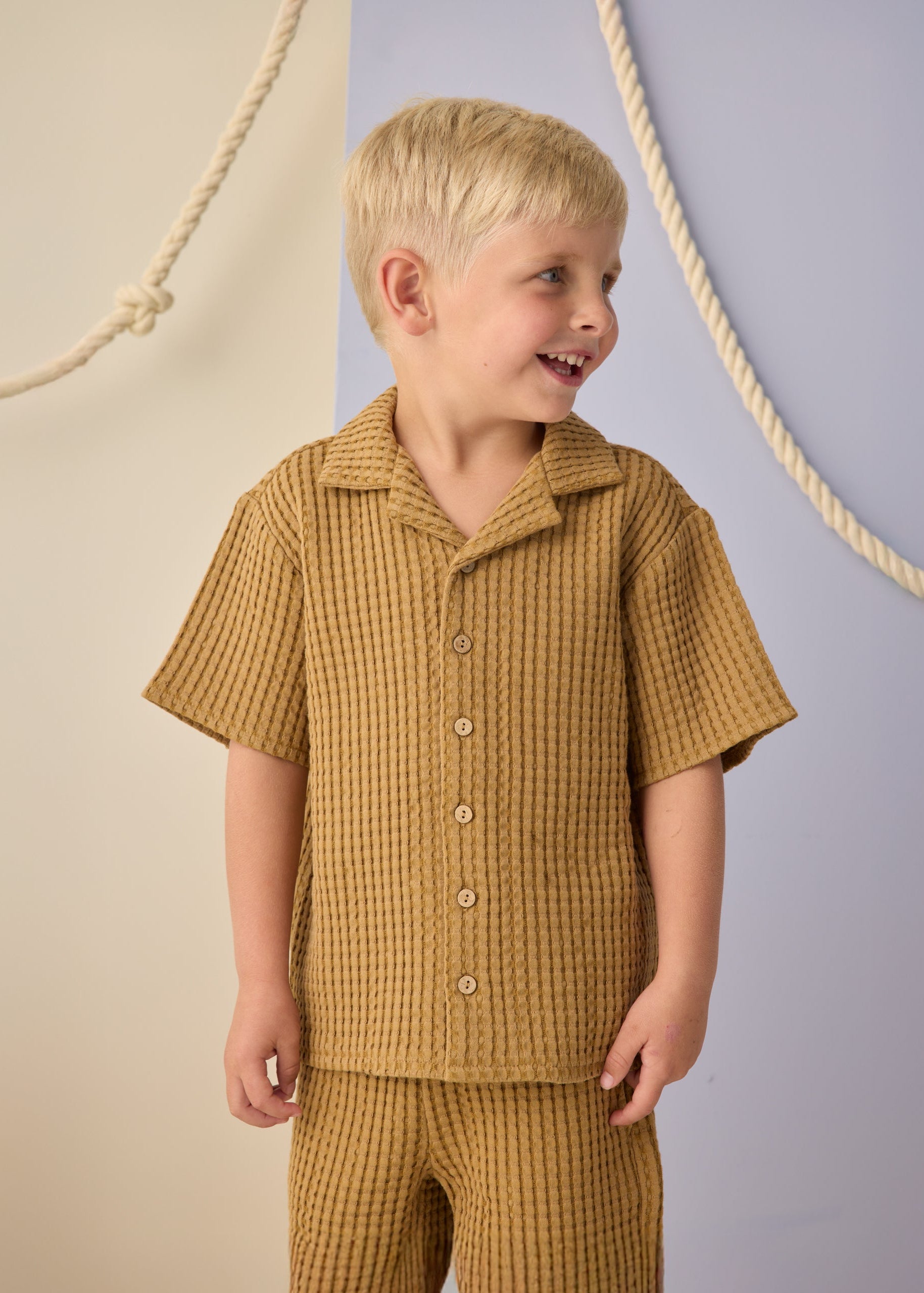 Child wearing a mustard yellow checkered outfit against a neutral background