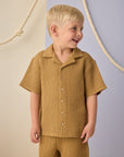 Child wearing a mustard yellow checkered outfit against a neutral background