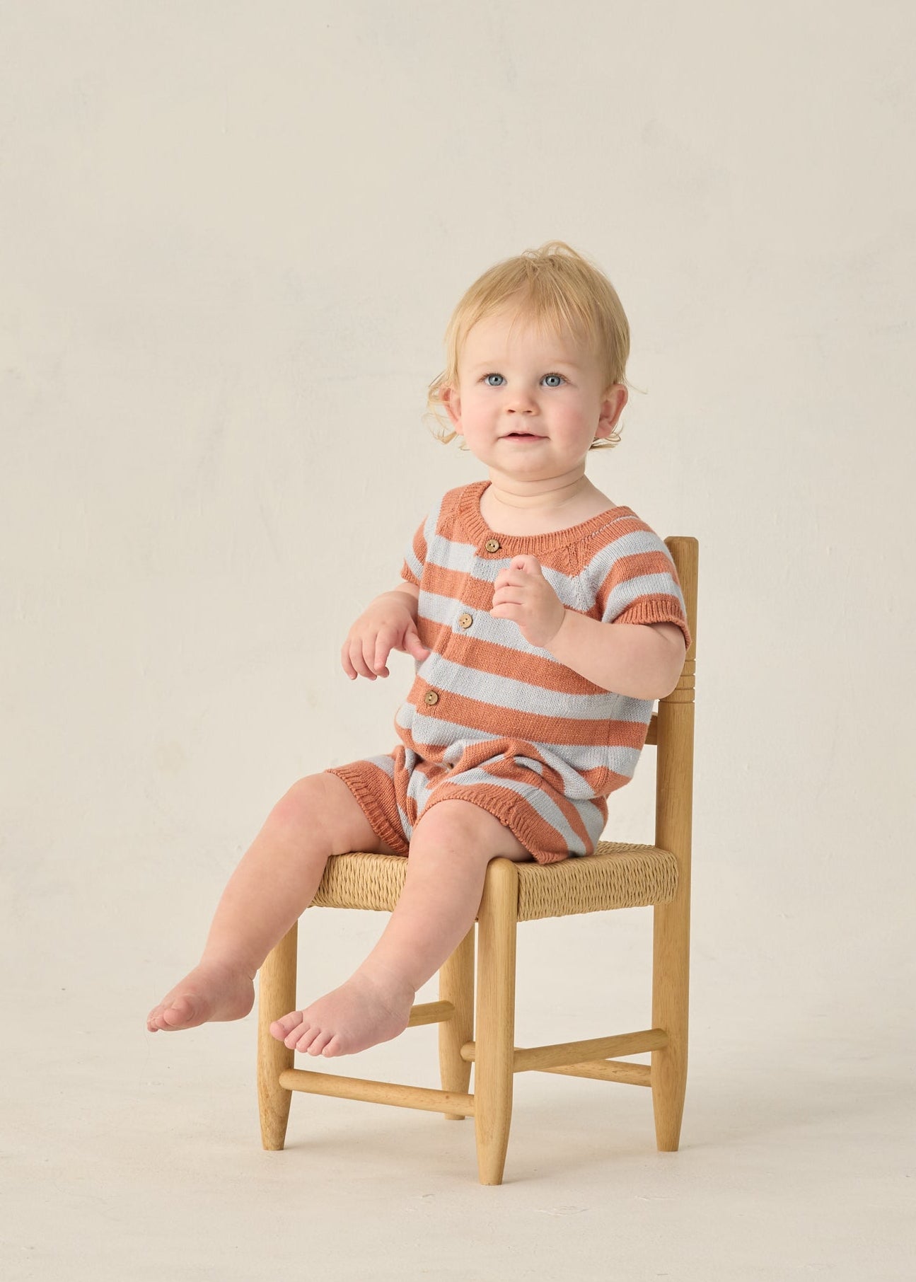 Child sitting on a small wooden chair against a plain background
