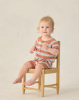Child sitting on a small wooden chair against a plain background