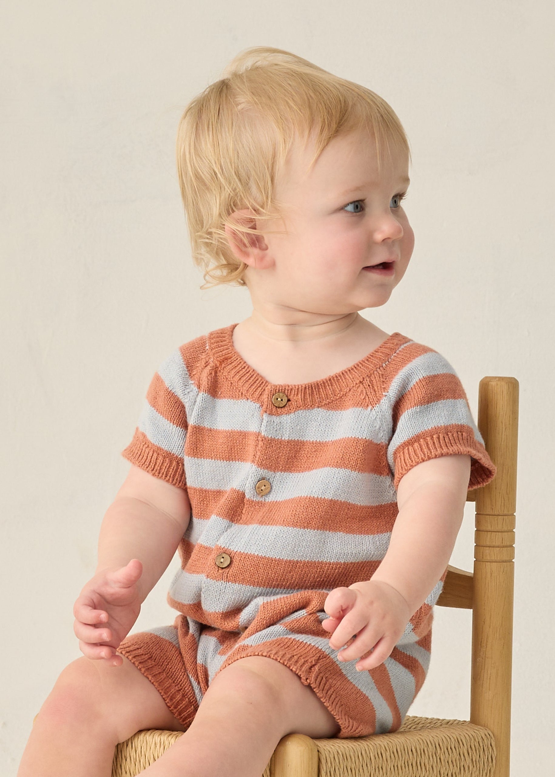 Baby wearing a striped orange and gray outfit sitting on a chair.