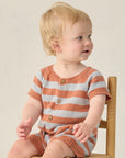 Baby wearing a striped orange and gray outfit sitting on a chair.