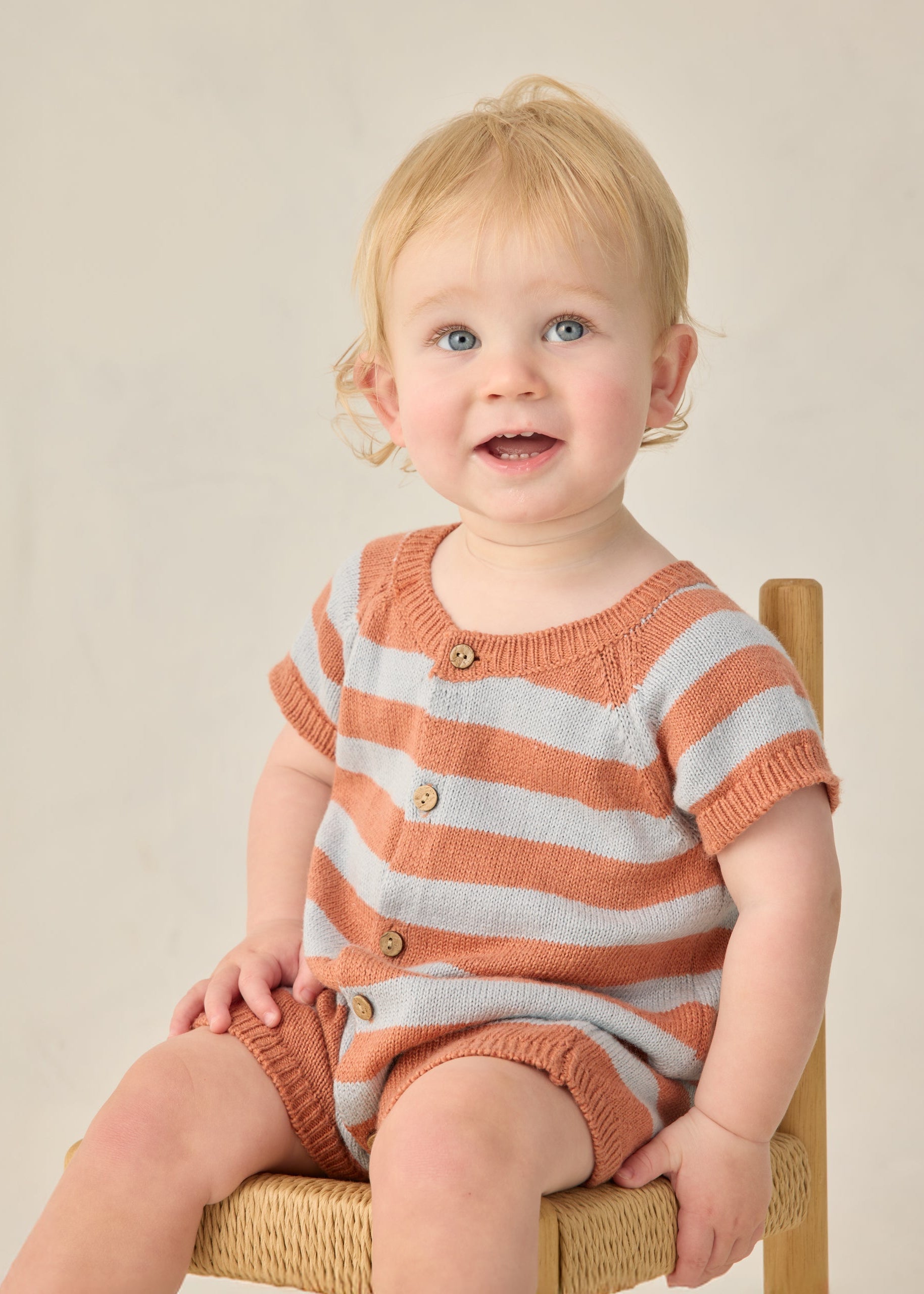 Child wearing a striped orange and white outfit sitting on a chair against a plain background