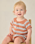 Child wearing a striped orange and white outfit sitting on a chair against a plain background
