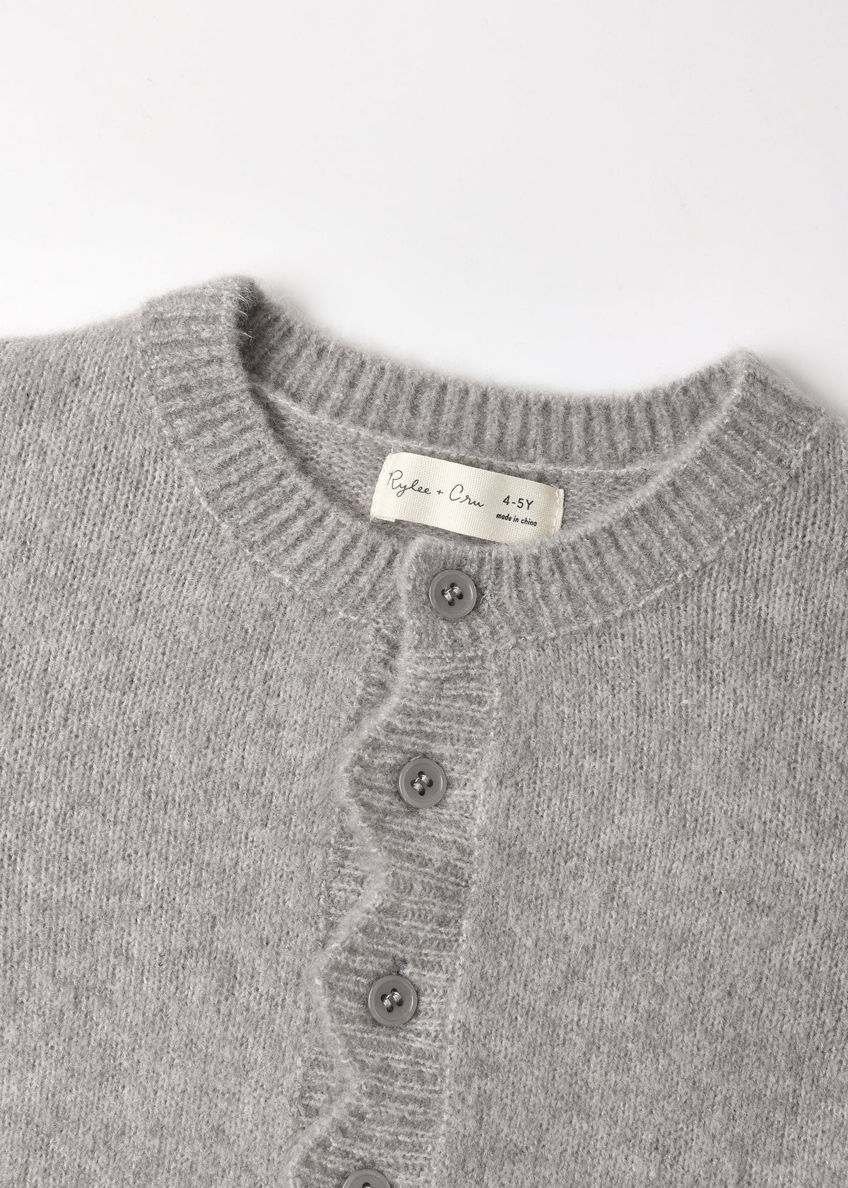 Close-up of a light gray knit cardigan sweater showing the ribbed crew neck, front buttons, and a cream-colored inner neck label that reads 'Cotton Club 439'.