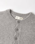 Close-up of a light gray knit cardigan sweater showing the ribbed crew neck, front buttons, and a cream-colored inner neck label that reads 'Cotton Club 439'.