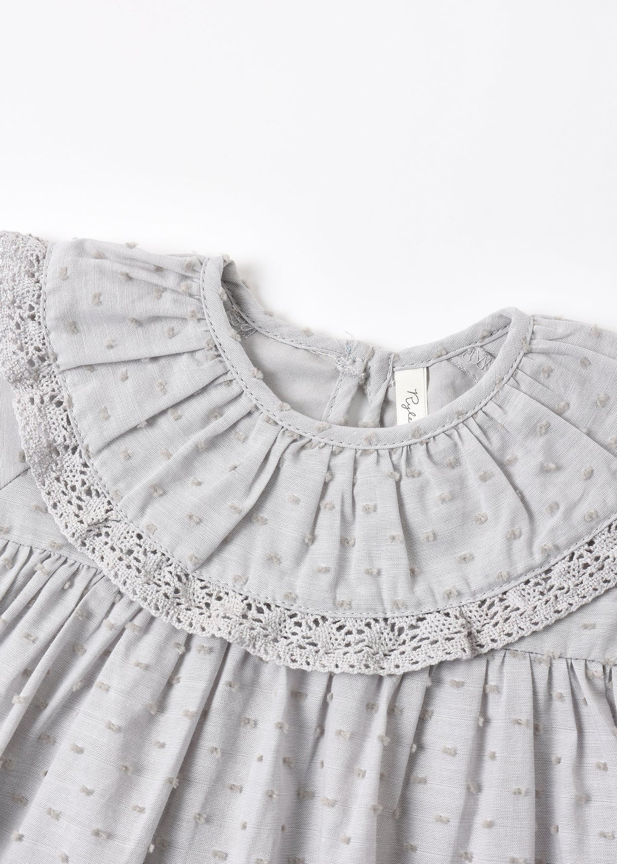 Close-up of a light gray baby dress featuring a textured fabric, a large pleated ruffled collar with delicate lace trim, and a small bow pattern.