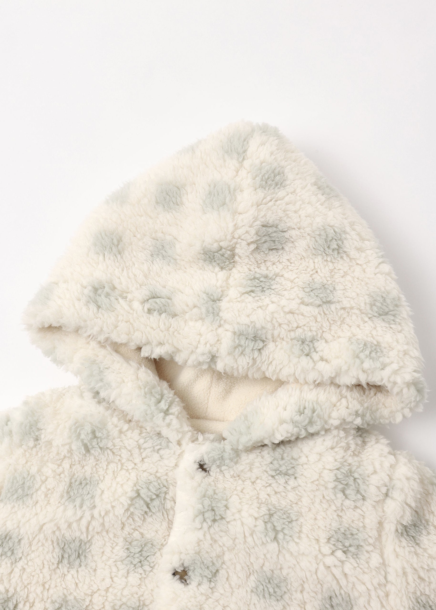 Close-up of a plush sherpa hooded jacket in cream with pale sage green polka dots, featuring a soft lining and snap-button closure.