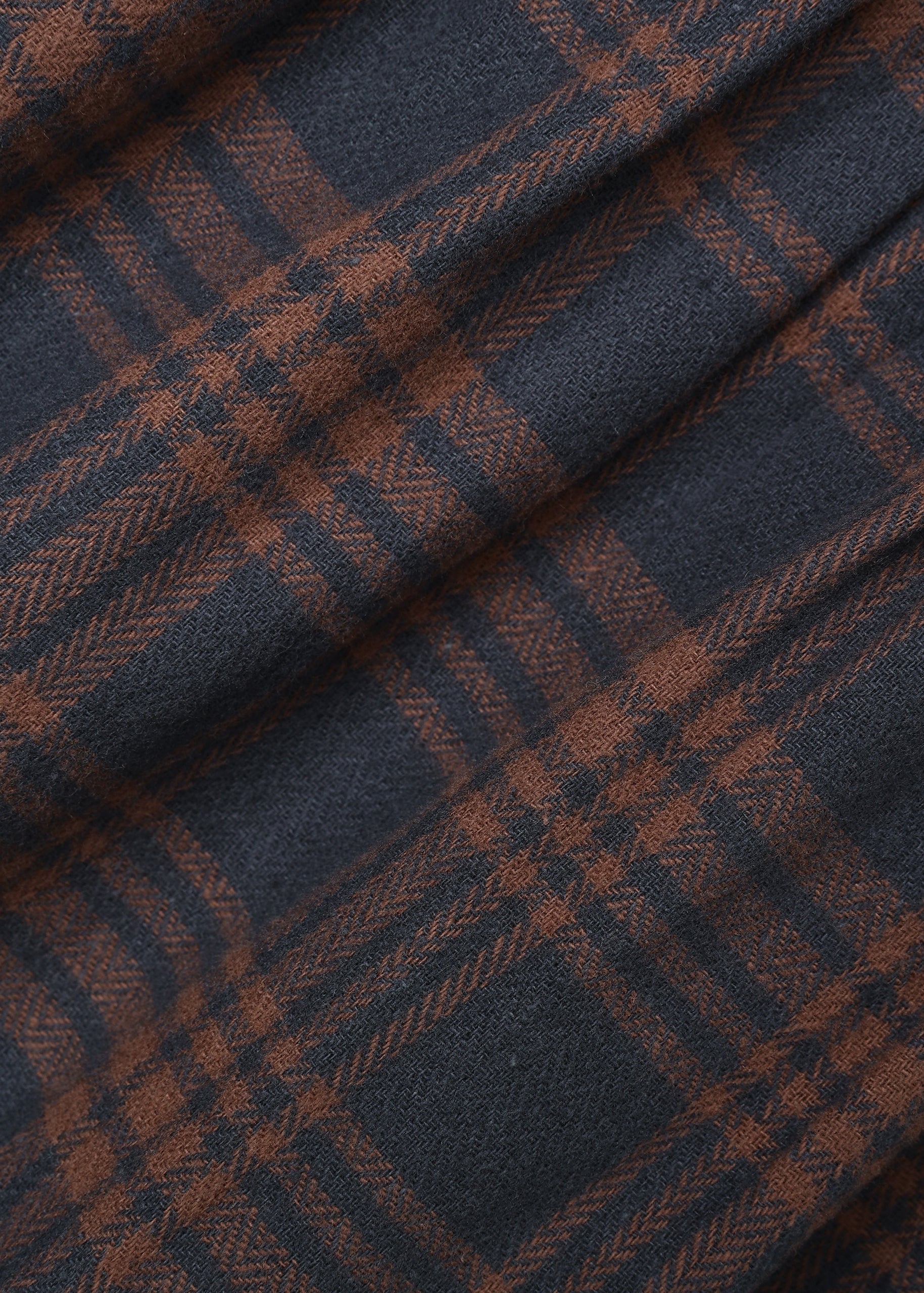 A close-up of a plaid fabric with a dark navy blue base and rust-brown intersecting stripes, showing a soft woven texture with elegant folds.