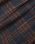 A close-up of a plaid fabric with a dark navy blue base and rust-brown intersecting stripes, showing a soft woven texture with elegant folds.