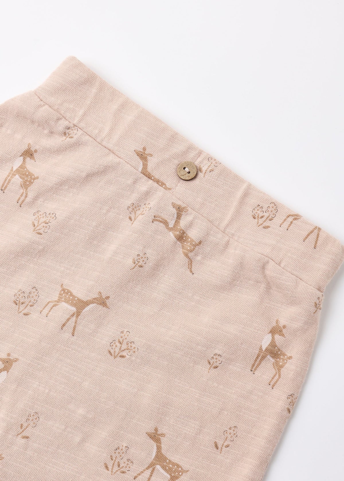 Close-up of a pair of light beige linen shorts with a brown deer and tree print, featuring a single wooden button at the waistband.