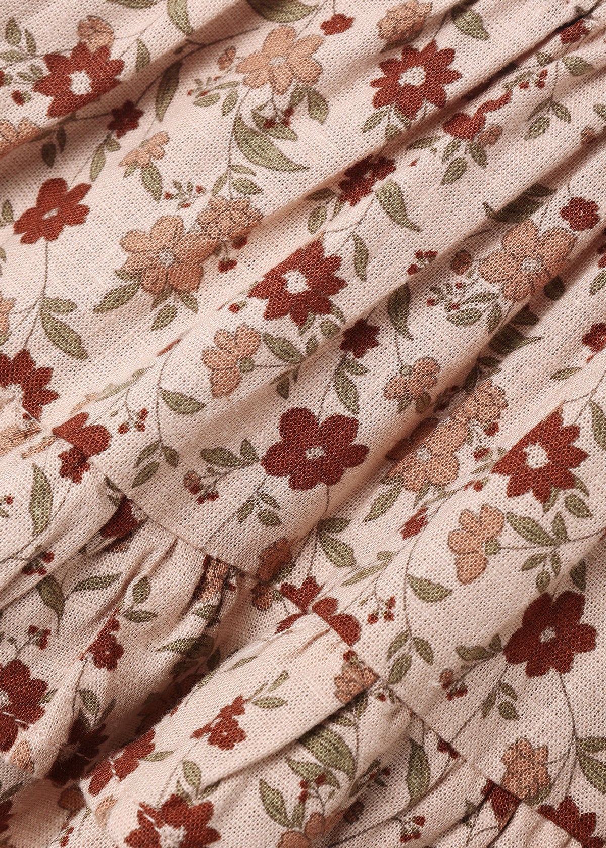 A close-up of a ruffled fabric with a vintage floral pattern in terracotta, dusty rose, and olive green on a warm beige background.