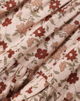 A close-up of a ruffled fabric with a vintage floral pattern in terracotta, dusty rose, and olive green on a warm beige background.
