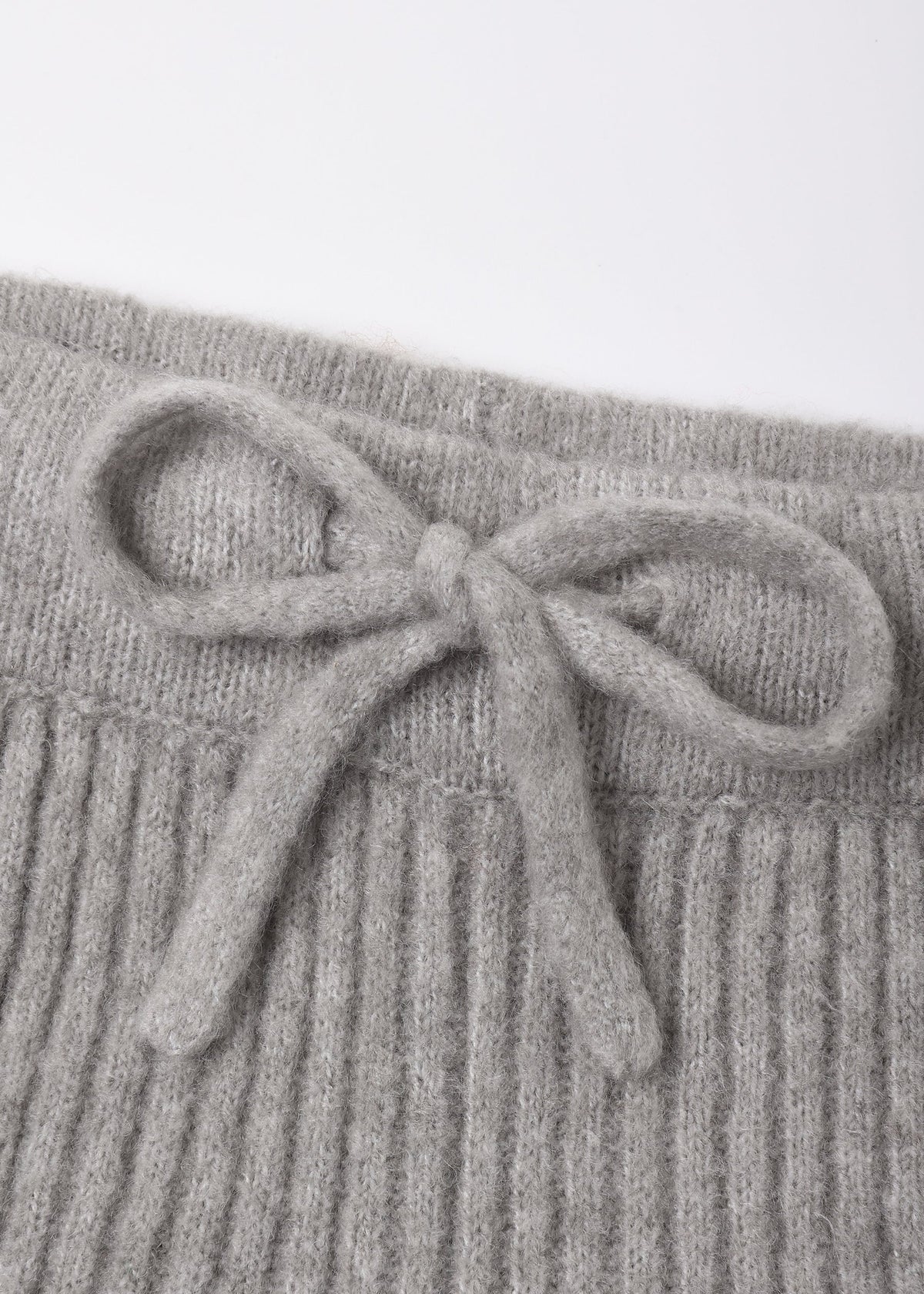 Close-up of a light gray ribbed knit garment with a matching fabric bow detail at the waistband, shown against a plain white background.