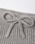 Close-up of a light gray ribbed knit garment with a matching fabric bow detail at the waistband, shown against a plain white background.