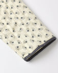 A close-up of a quilted blanket or comforter with a cream-colored background and a repeating pattern of small gray and black floral motifs, finished with a dark gray piped edge.