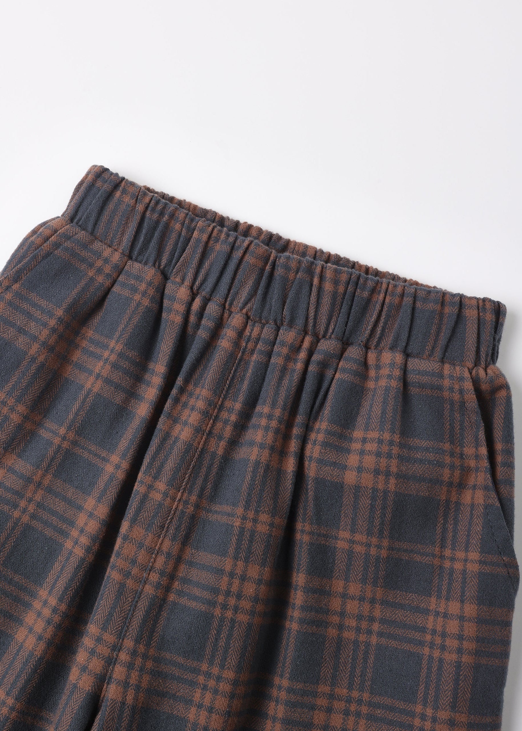 Close-up of a plaid skirt with an elastic waistband, featuring a dark gray and rust brown tartan pattern, shot against a plain white background.