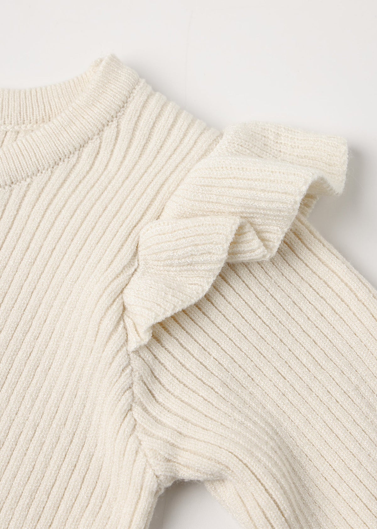Close-up of a cream ribbed knit garment with a ruffled shoulder detail, shown against a plain light background.