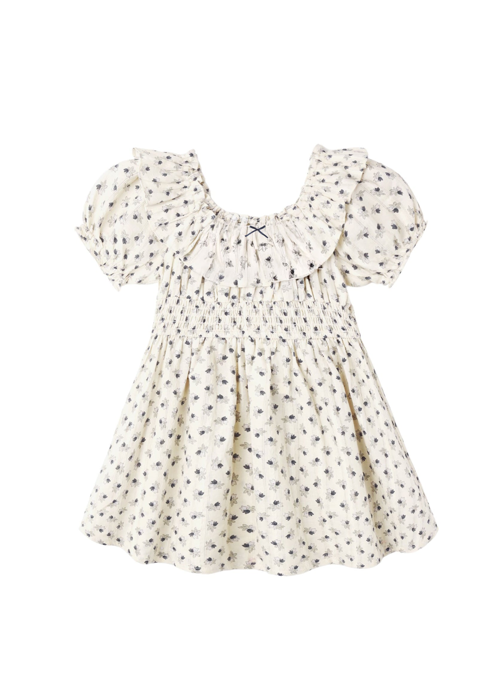 A cream-colored baby dress with a small black floral pattern, featuring a smocked bodice, ruffled collar, and short puff sleeves, shown against a plain white background.
