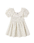 A cream-colored baby dress with a small black floral pattern, featuring a smocked bodice, ruffled collar, and short puff sleeves, shown against a plain white background.
