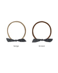 Two fabric hair ties on a white background, one in beige and one in brown, each with a dark gray bow at the bottom and text labels underneath.