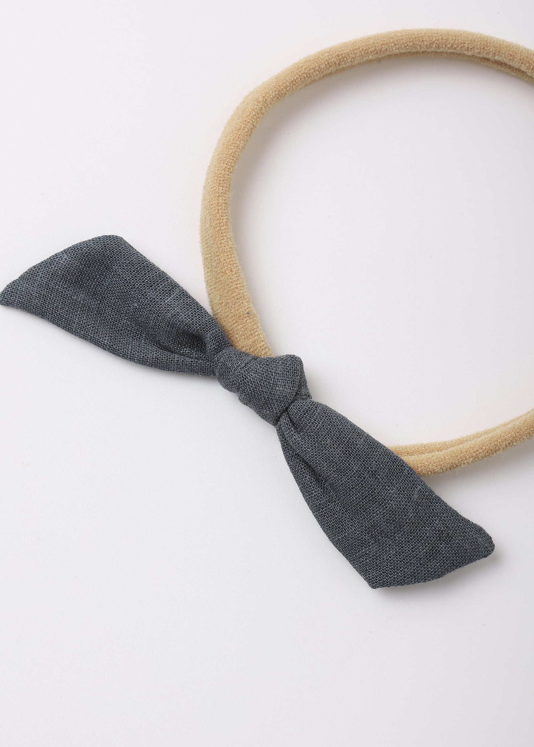 A beige fabric headband with a dark gray fabric bow tied at the front, photographed on a clean white background.
