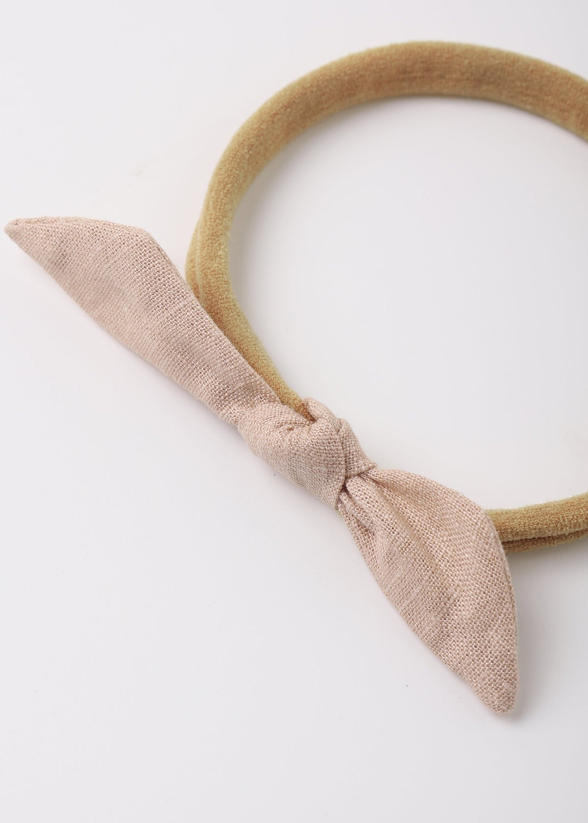 A beige fabric headband with a knotted bow detail, photographed on a clean white background.