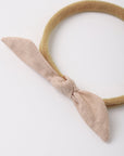 A beige fabric headband with a knotted bow detail, photographed on a clean white background.
