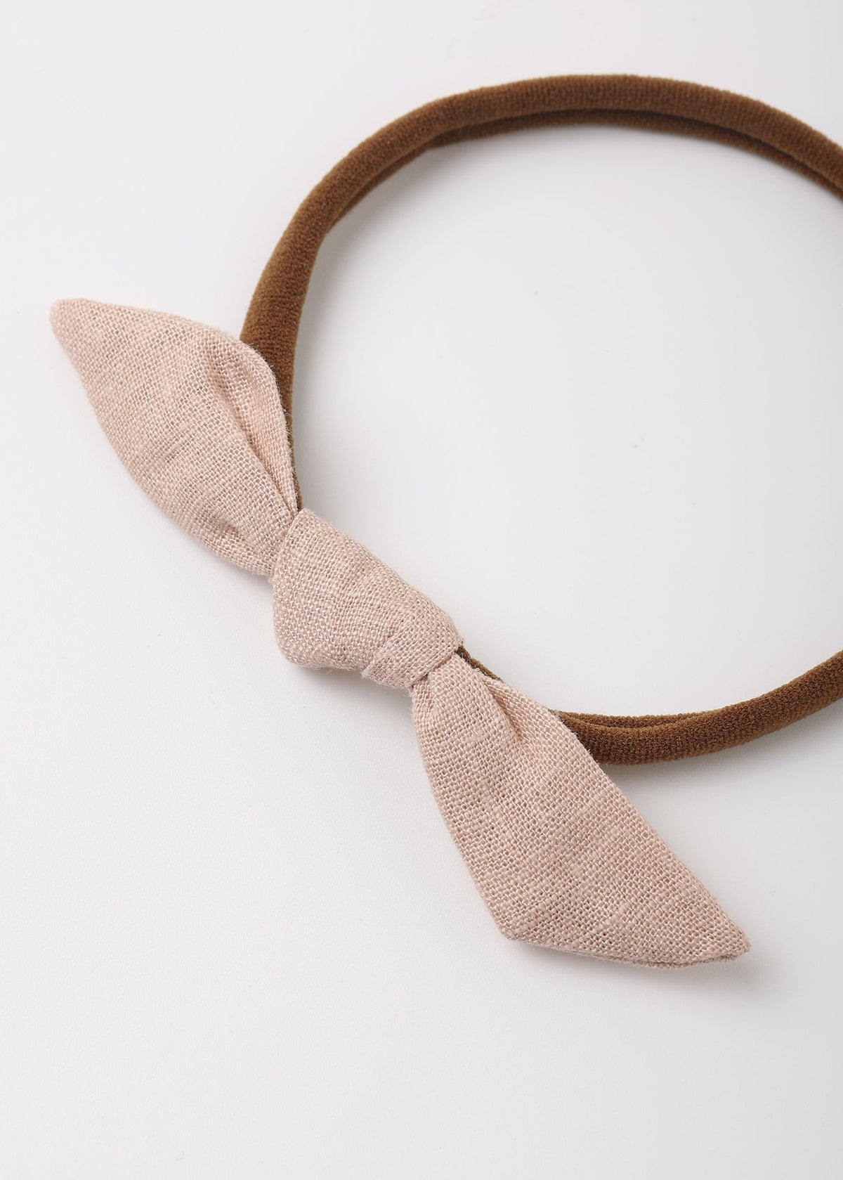 A brown elastic headband featuring a large, textured light beige fabric bow on the front, photographed on a clean white background.