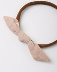 A brown elastic headband featuring a large, textured light beige fabric bow on the front, photographed on a clean white background.