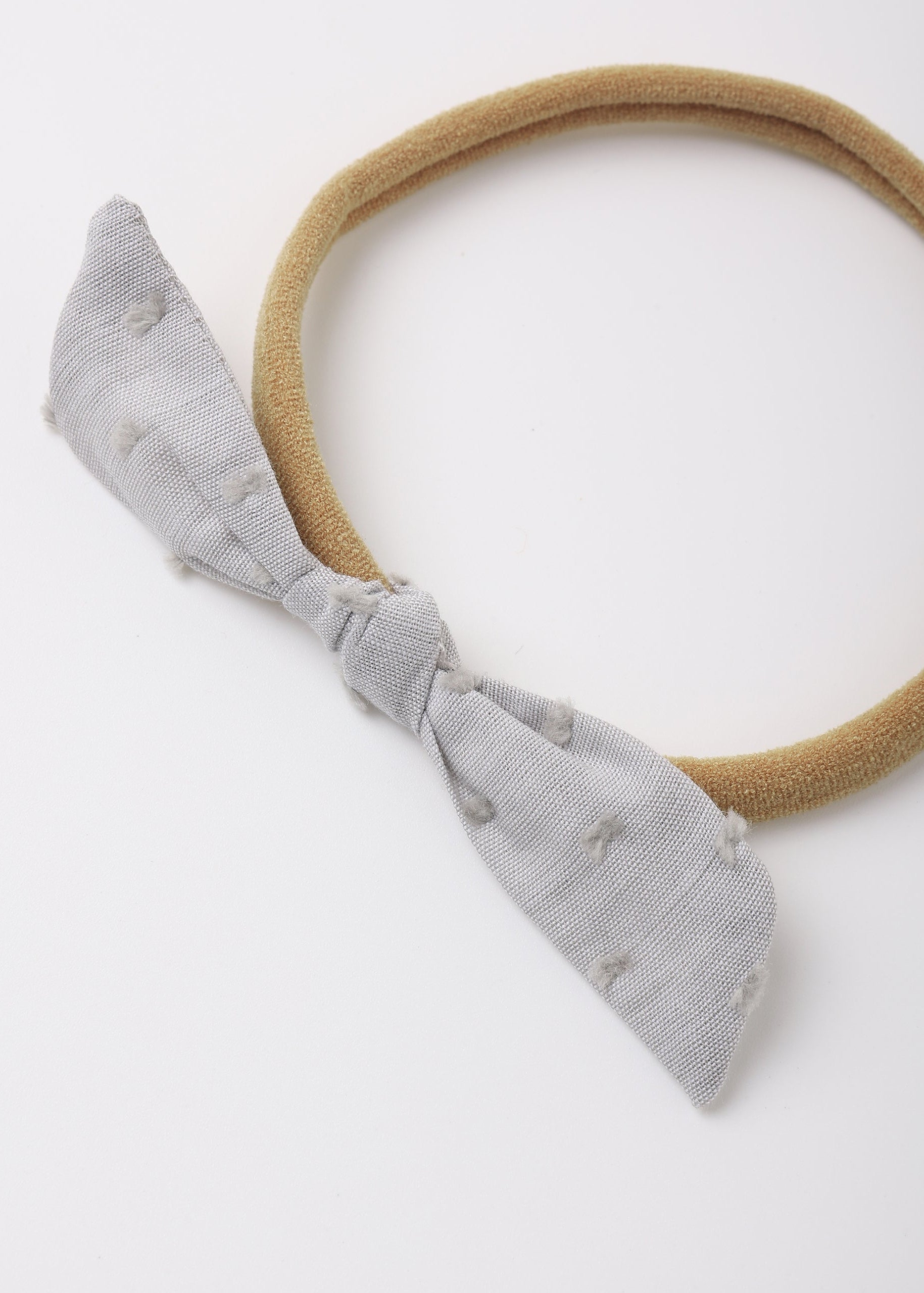 A light gray textured fabric bow headband with a tan elastic band, photographed on a clean white background.