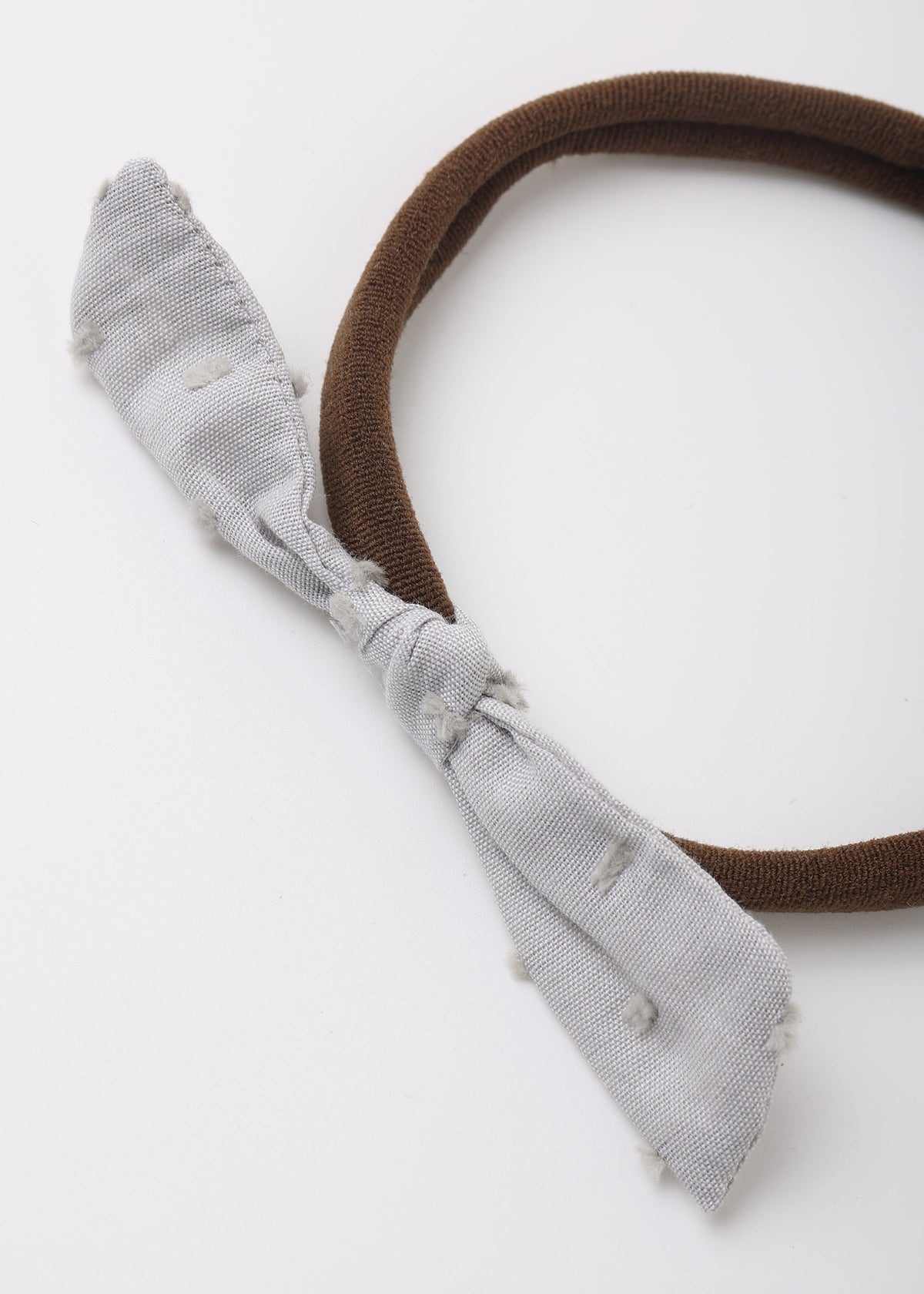 A brown fabric headband with a knotted bow in a light gray, distressed denim-like fabric, shown on a plain white background.
