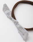 A brown fabric headband with a knotted bow in a light gray, distressed denim-like fabric, shown on a plain white background.