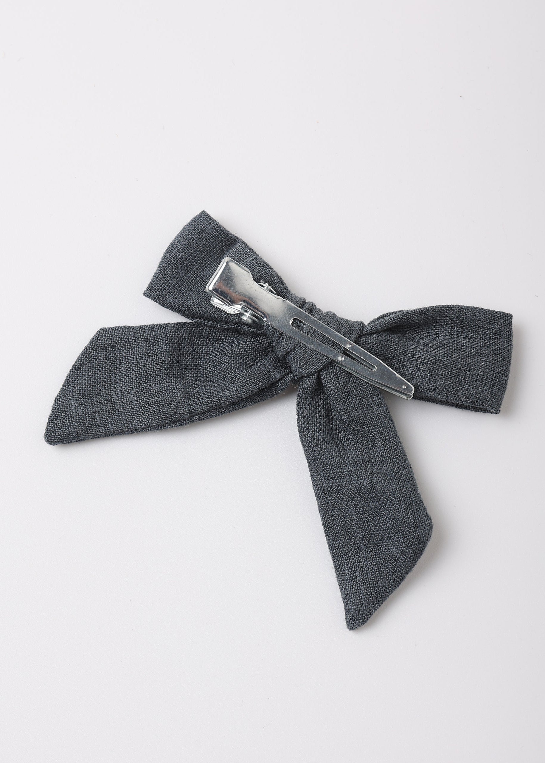 A dark gray textured fabric hair bow with a silver metal spring clip, photographed on a clean white background.