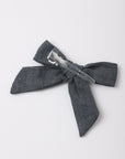 A dark gray textured fabric hair bow with a silver metal spring clip, photographed on a clean white background.