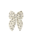 A cream-colored fabric hair bow with a delicate gray floral pattern, photographed flat against a solid white background.