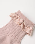 A close-up of a light pink ribbed knit sock with a matching pink crochet lace ruffle trim at the cuff, shown on a plain white background.
